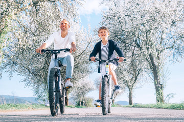 Fototapeta premium Father and son having fun when riding bicycles on country road under blossom trees. Healthy sporty lifestyle concept image.