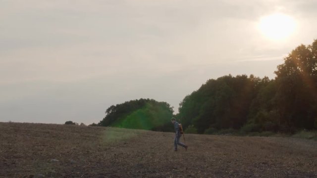 A young man with guitar wanders across a scenic field at golden sunset