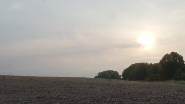 A lost young man with guitar wanders across the field at golden sunset