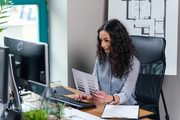 Young business woman holds color palette and works at computer in modern office.