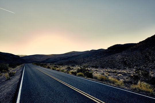 paved desert road leading into horizon at sunset