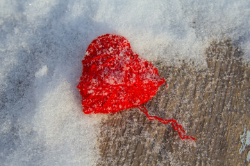 Red knitted heart on a snow-covered wooden surface. St. Valentine's Day