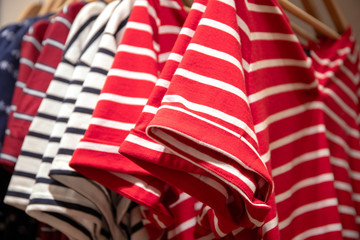 Striped shirts on hangs for sale in shop. Red and white polo on wooden hanger. Summer seasonal wear in department store
