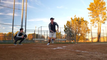 Amateur baseball player uses his bat to bit a bunt during a game on a public park field over home plate in spring time in America. - Powered by Adobe