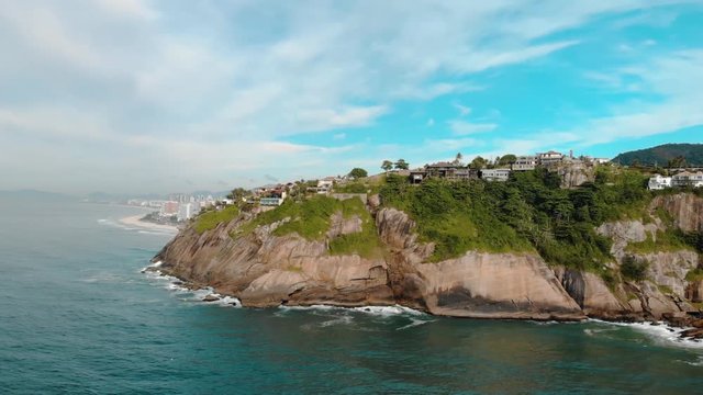 Full panoramic aerial view of Joatinga beach in Rio de Janeiro with its cliff rocks at high tide, a small beach, the Gavea mountain behind it and in the distance left well known landmarks of the city