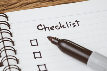 Selective focus on handwriting headline the word Checklist with black marker pen and check box on small notepad on wood table, to do list, prioritize or reminder for project or plan