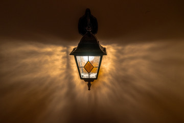 Old  glass lantern on orange plastered wall with shadows in the dark