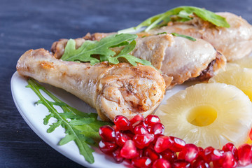 Fried chicken legs with rucola, pineapple and pomegranate seeds on black wooden background.