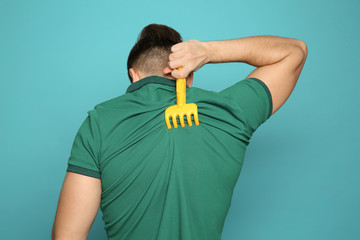 Young man scratching back with toy rake on color background. Annoying itch