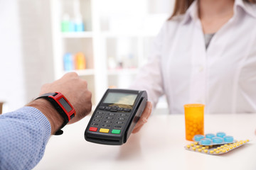 Man using terminal for contactless payment with smart watch in pharmacy, closeup. Space for text