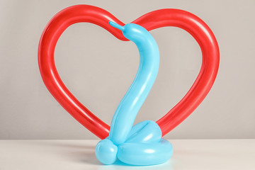 Snake and heart figures made of modelling balloons on table color light background