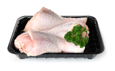 Plastic container with raw chicken drumsticks and parsley on white background. Fresh meat