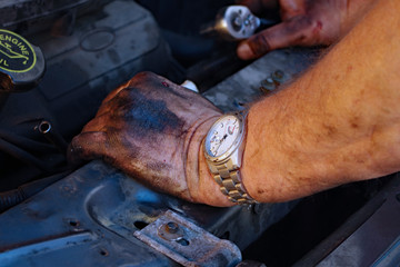 Grease covered hands of an automotive mechanic with a small bleeding cut