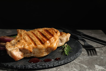 Grilled meat served with rosemary and sauce on slate plate against black background. Space for text