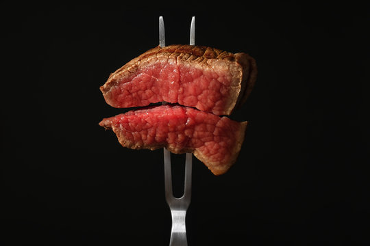 Carving fork with pieces of steak on black background. Tasty meat