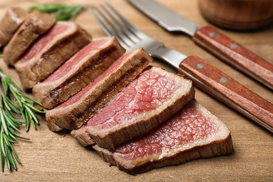 Cut roasted meat with rosemary on wooden background, closeup