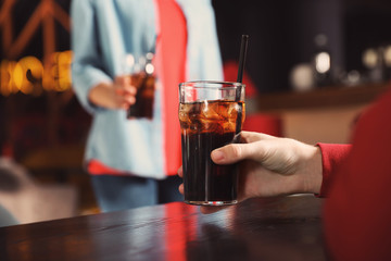Man holding glass of cola at table in bar, closeup. Space for text