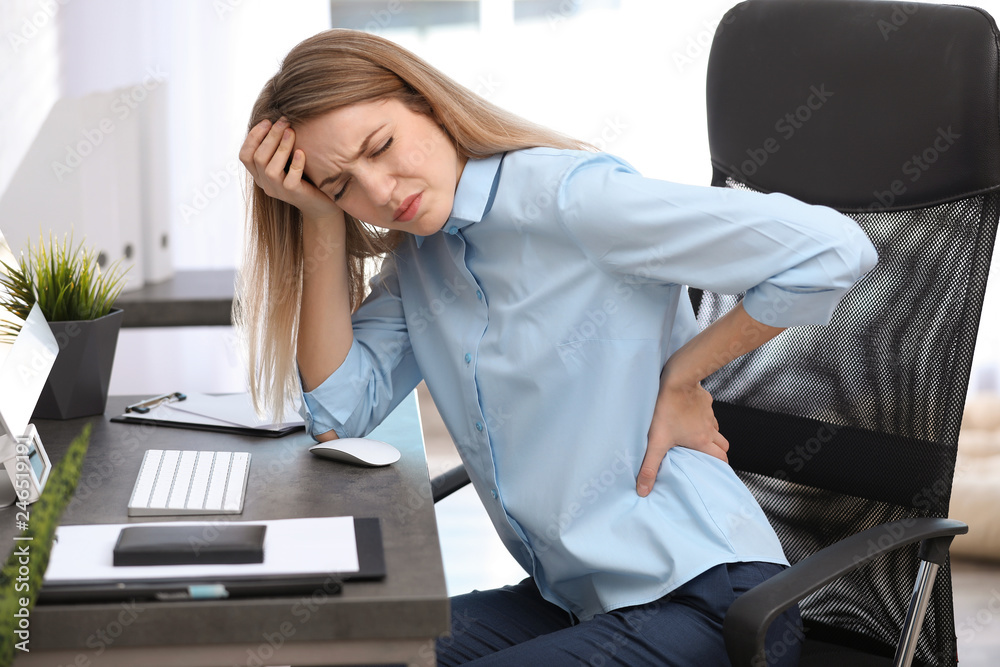 Wall mural young woman suffering from back pain in office