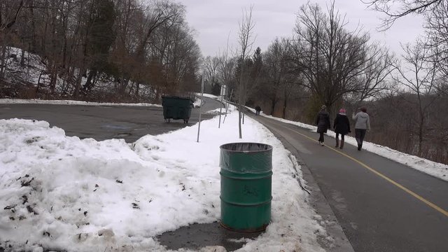 4K Trash Cans In Park With Snow And Girls Pedestrians Walking By