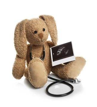 Ultrasound photo of baby and toy rabbit on white background. Concept of pregnancy