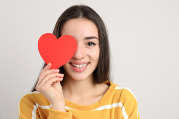 Portrait of beautiful young woman with paper heart on light background