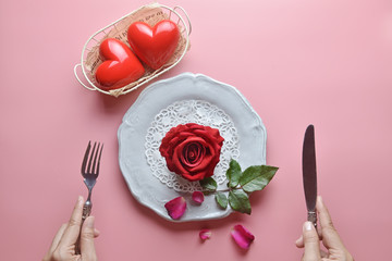 Red rose on white dish, with hand holding fork and knife, And couple heart in white basket, On pink background, Concept of Valentine's Day, Romance, Love, dinner, Special day