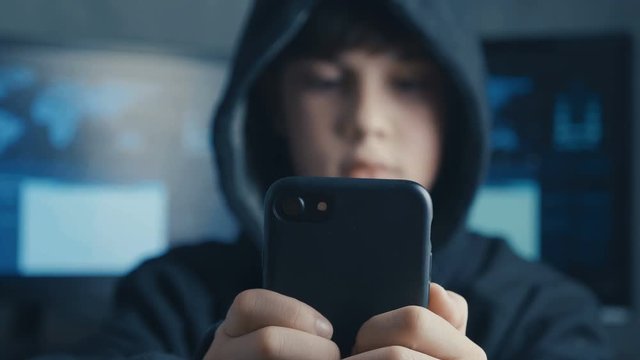 Young hooded boy using a smartphone device. Portrait of Genius boy wonder hacks system at cyberspace.