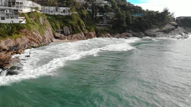 Slow moving aerial view of the ocean waves coming in rolling hitting the cliff rocks of Joatinga beach in Rio de Janeiro
