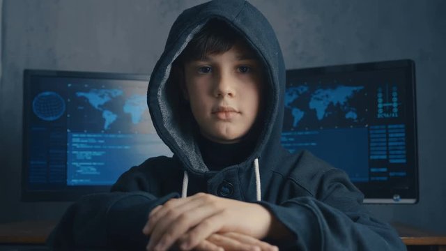 Boy wonder Hacker in hood at data center filled with display screens. Portrait of Child prodigy hacker.
