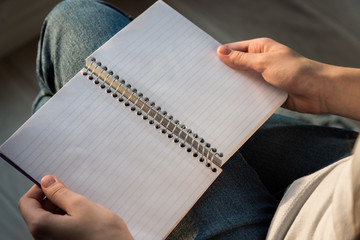 Woman holding spiral bound notebook with lined paper in lap, sitting in sunlight