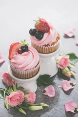 Cupcakes with on porcelain stands with rose flowers on a white background. Spring dessert concept with copy space