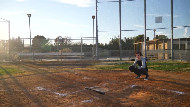 A young man baseball player hits a bunt with his bat and runs to first base during a team practice in the park at sunset.