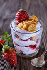 Dessert trifle, cooked at home, with strawberries and orange slices with thick curd cream in a glass beaker on a wooden table