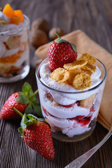 Dessert trifle, cooked at home, with strawberries and orange slices with thick curd cream in a glass beaker on a wooden table