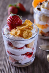 Dessert trifle, cooked at home, with strawberries and orange slices with thick curd cream in a glass beaker on a wooden table