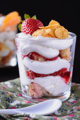 Dessert trifle, cooked at home, with strawberries and orange slices with thick curd cream in a glass beaker on a dark background, closeup