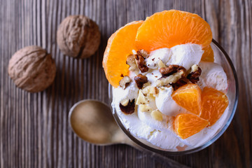 Dessert trifle, cooked at home, with orange slices and thick curd cream and nuts in a glass beaker on a wooden table, top view