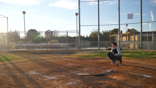 A young man baseball player hits a home run and then runs to first base during a team practice in the park at sunset.