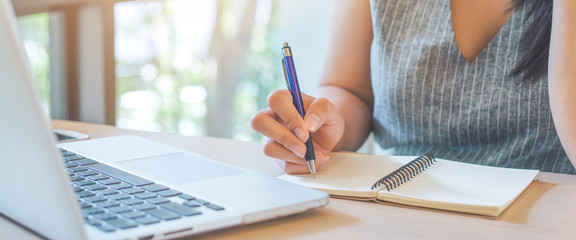 Woman hand is writing on notepad with pen in office.