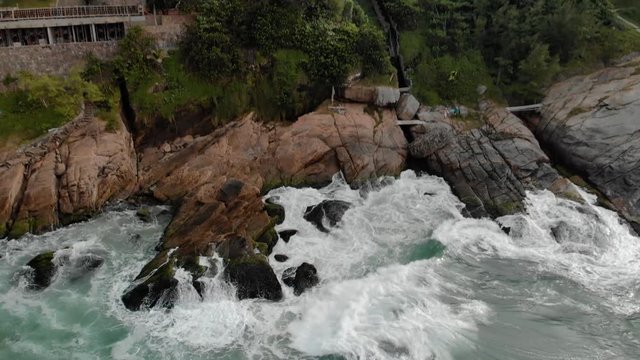Approaching aerial view of the ocean waves rolling in hitting the cliff rocks of Joatinga beach in Rio de Janeiro