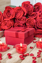 Festive background to the Valentine's day. A bouquet of red roses, a gift box and a heart-shaped candle. On a wooden background.