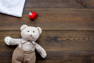 Baby care. Newborn baby concept. Teddy bear toy near pacifier on dark wooden background top view copy space