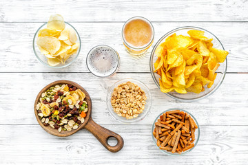 Snacks and beer. Chips, nuts, rusks near beer on white wooden background top view