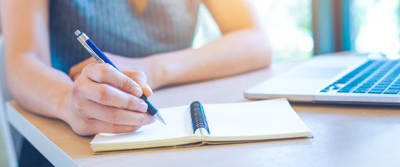 Woman hand is writing on notepad with pen in office.