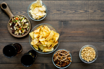 Fast food for TV watching. Snacks on desk.  Chips, nuts, rusks and soda on dark wooden background top view copy space