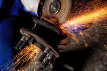 A close-up of a car mechanic using a metal grinder to cut a car part  in an auto repair shop, bright orange flashes flying in different directions, in the background tools for an auto repair