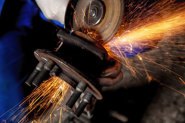 A close-up of a car mechanic using a metal grinder to cut a car part  in an auto repair shop,...