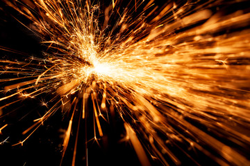 Bright orange and yellow sparks on a black background. A stream of bright sparks from metal cutting