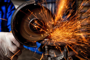 Close-up of a man sawing metal with a hand circular saw,  bright flashes flying in different directions, in the background tools for an auto repair shop. Work of auto mechanics.