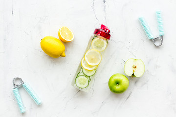 Healthy fruit water for sport, fitness. Bottle of water with lemon and cucumber near sport equipment on white stone background top view